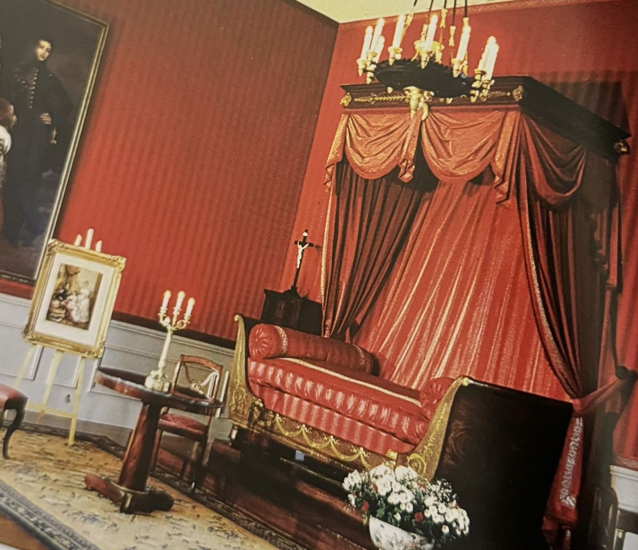 An ornate room with red damask walls and a gilded canopy bed